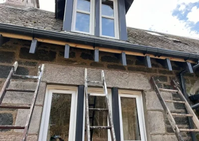 Roof moss removal ladders set up on stone residential property